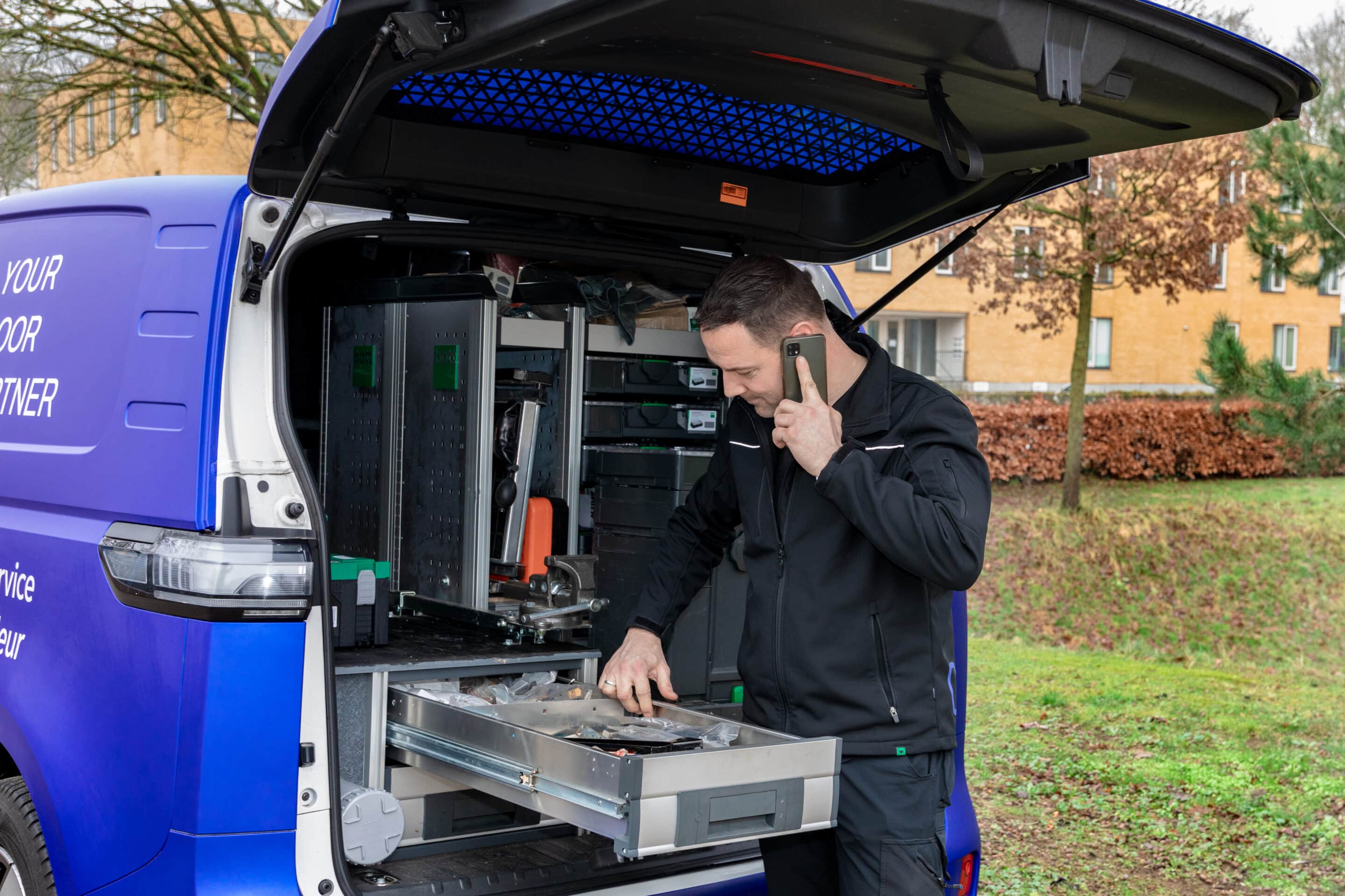 Monteur met pak spullen uit de monteursbus terwijl hij belt